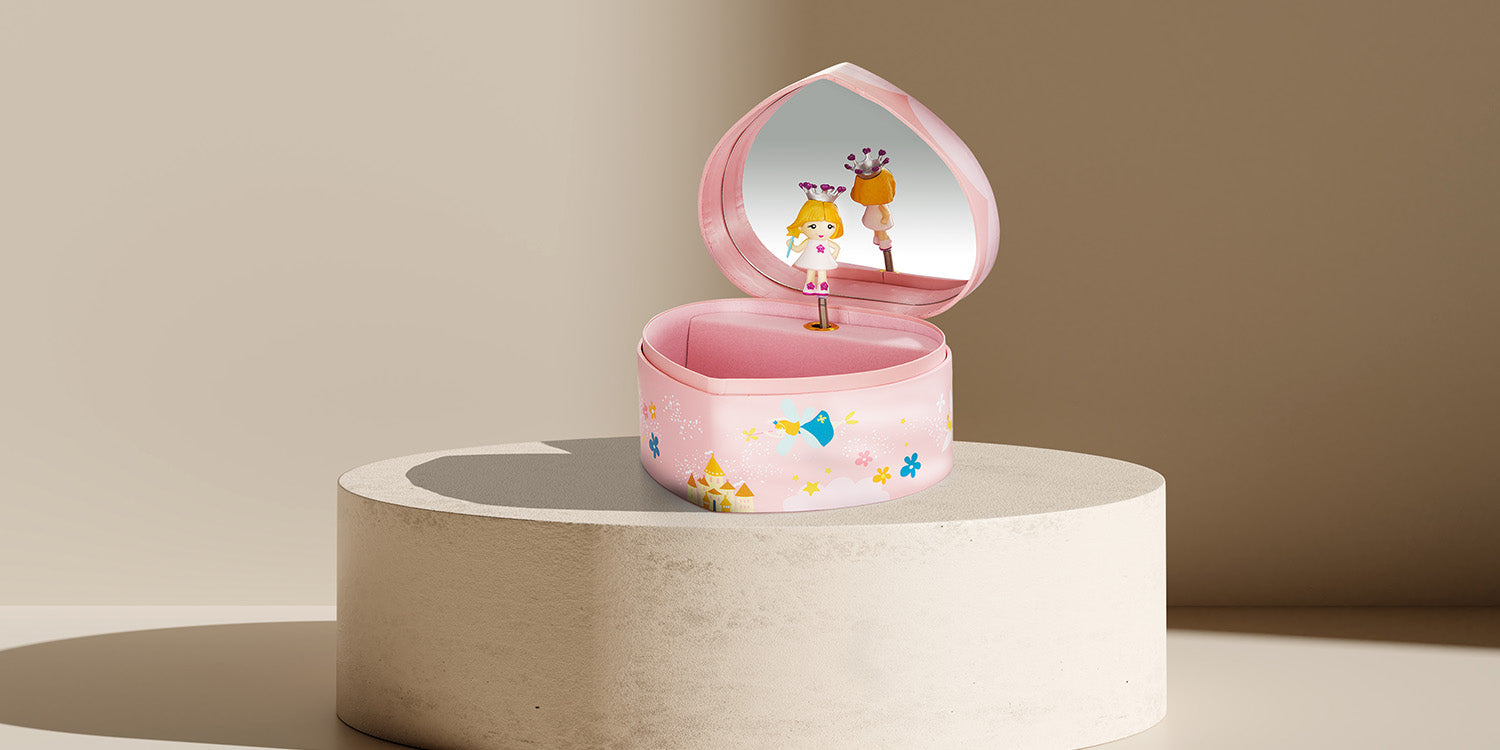 Rosa Kinder-Schmuckdose in Herzform mit Spieluhr und tanzender Ballerina-Figur im Inneren, verziert mit bunten Märchen-Motiven wie Vögeln und Blumen, präsentiert auf modernem beigem Podest