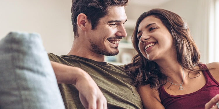 Glückliches Paar entspannt auf dem Sofa - Frau trägt silberne Halskette mit Herz-Anhänger, Mann in olivgrünem Shirt