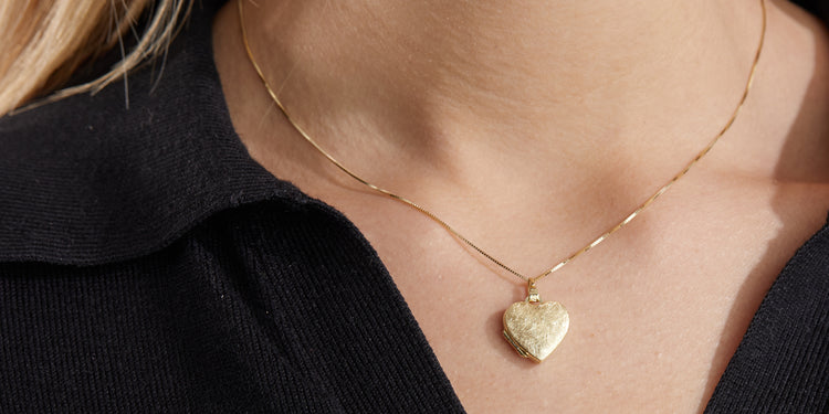 Goldene Halskette mit herzförmigem Medaillon am Dekolleté getragen