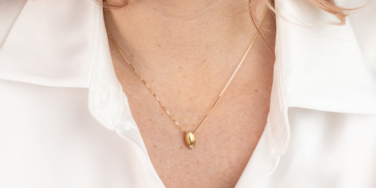 Goldene Halskette mit tropfenförmigem Anhänger am Dekolleté getragen