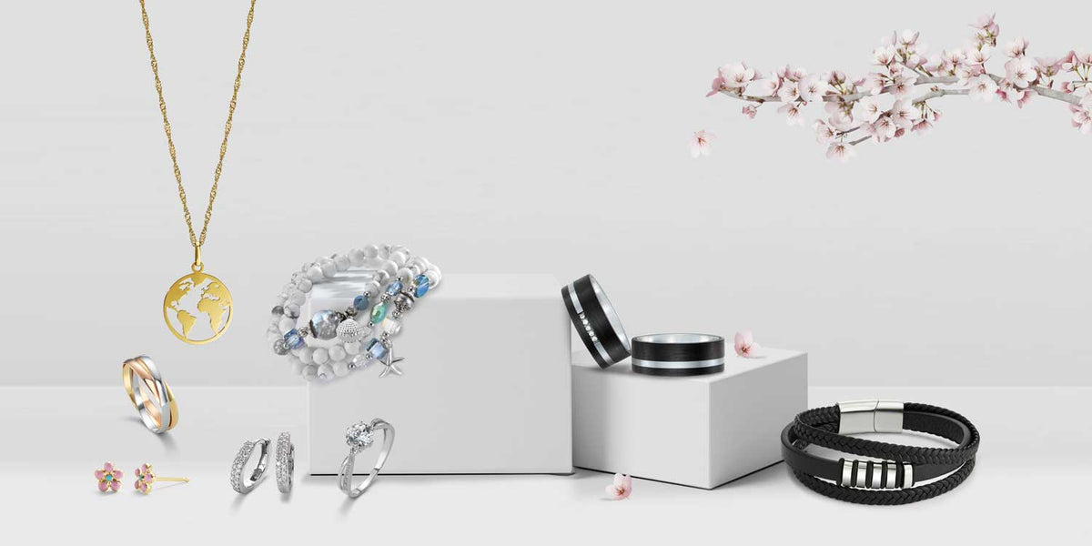 Schmuck-Kollektion mit goldener Weltkarten-Halskette, silbernen Ringen, bunten Ohrringen, Perlenarmband und schwarzem Lederarmband auf weißem Hintergrund mit Kirschblüten