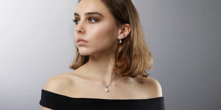 Frau mit schulterlangem braunem Haar trägt elegante Perlen-Ohrringe und eine zarte Perlenkette zu einem schwarzen schulterfreien Top